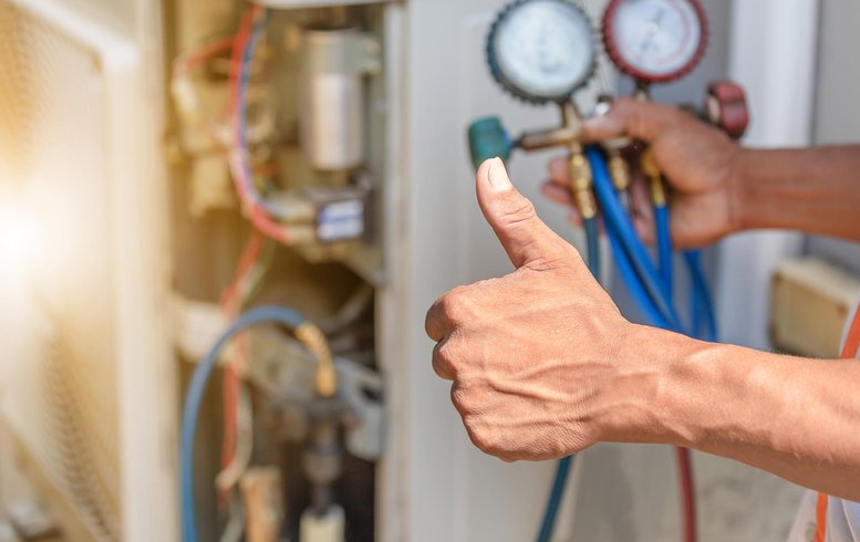 Un technicien effectuant des réglages sur un système de climatisation, avec des manomètres et des tuyaux en place. Le geste de pouce levé indique que l'entretien est réussi et que le système fonctionne correctement.