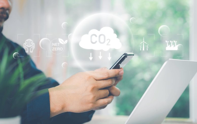 Un individu utilisant un téléphone mobile, avec des icônes numériques représentant des éléments liés à la durabilité et à la réduction du CO2, tels que des symboles de l'énergie renouvelable et de l'objectif net zéro. L'écran de l'ordinateur portable à côté suggère une analyse de données environnementales.