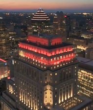 Vue aérienne nocturne du centre-ville de Montréal avec l’édifice Sun Life illuminé en rouge au premier plan et les gratte-ciel environnants brillamment éclairés à la tombée du jour.