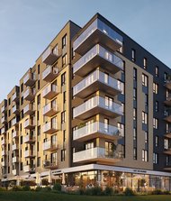 Immeuble résidentiel moderne de plusieurs étages avec balcons vitrés et commerces au rez-de-chaussée, baigné par la lumière du coucher du soleil. L’environnement est verdoyant et calme.