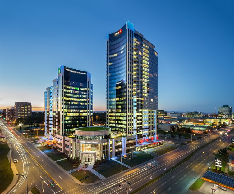 Aerial view of  Complexe Jules-Dallaire. A modern office tower complex lit up at dusk, bordered by wide avenues and surrounded by commercial buildings.